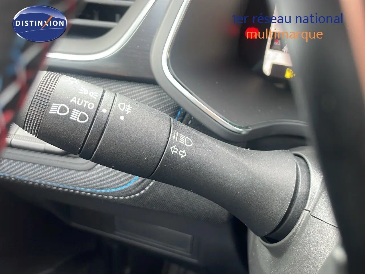 Gros plan sur la commande des phares et clignotants du Renault Captur E-Tech gris cassiopée avec surpiqûres bleues à l'intérieur.