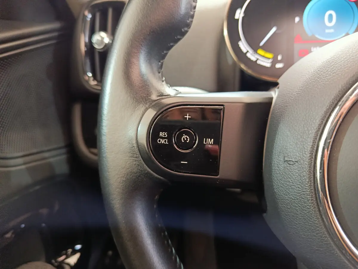 Gros plan sur les commandes de régulateur de vitesse au volant cuir noir d’un MINI Countryman hybride blanc.