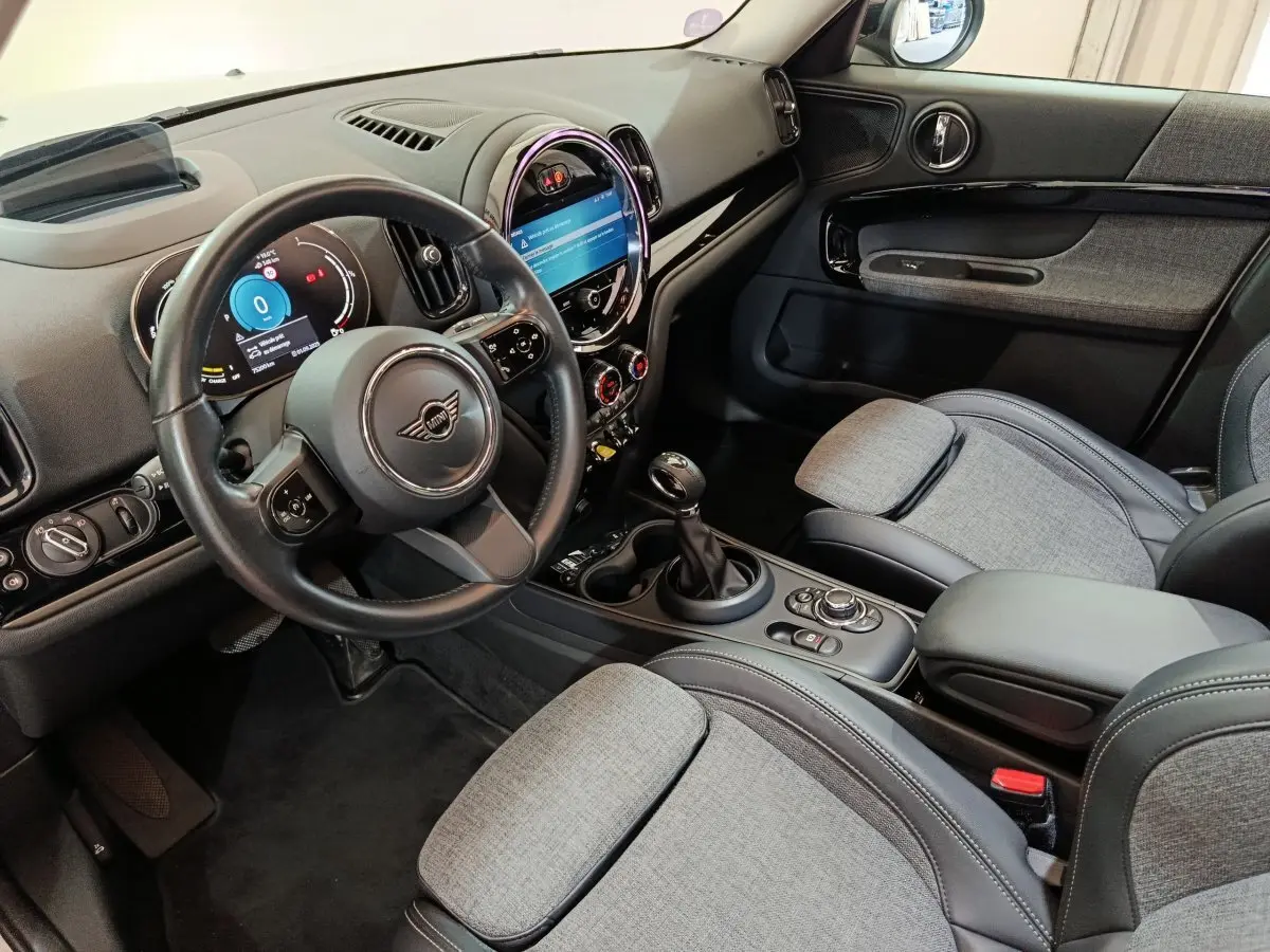 Intérieur avant droit du MINI Countryman blanc 2021, tableau de bord avec écran tactile rond et sièges gris tissu et cuir.