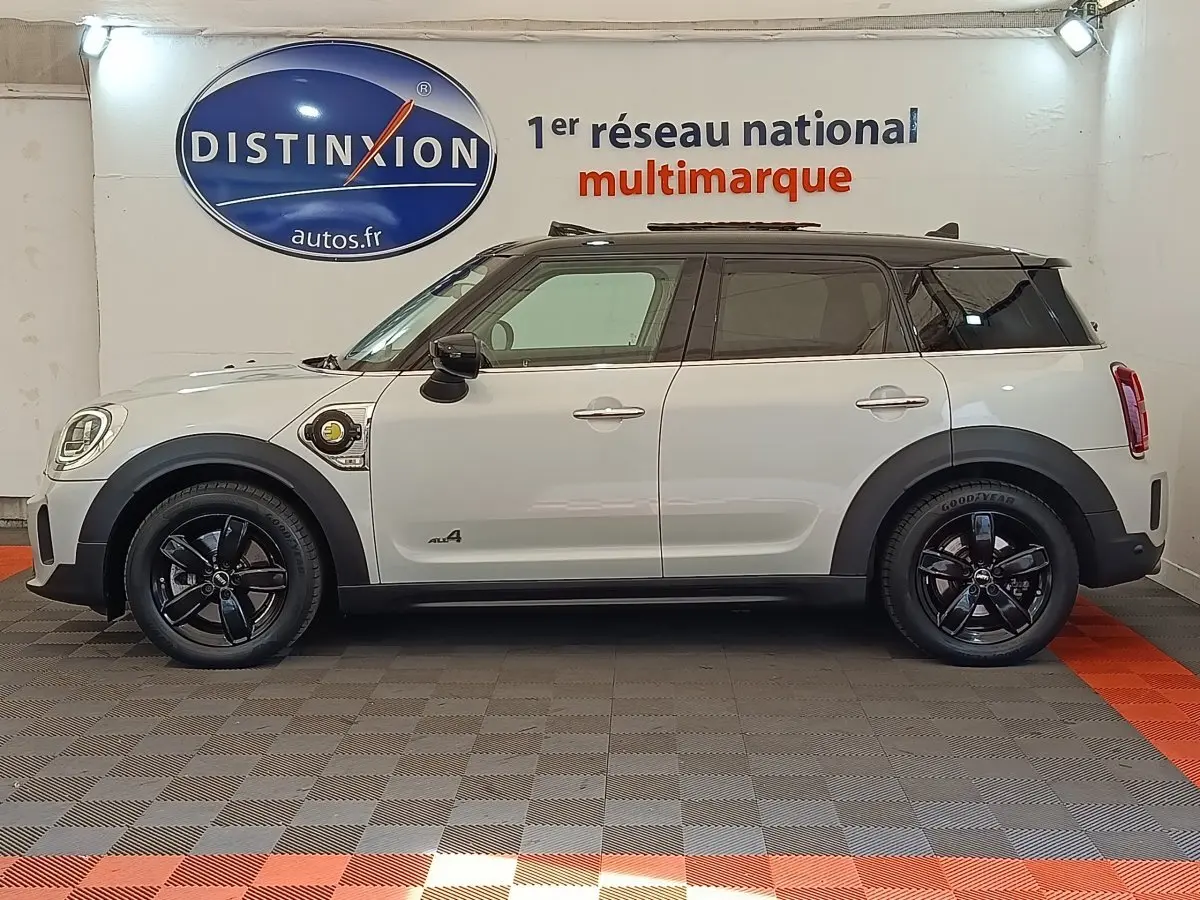 Vue de profil côté gauche d'un MINI Countryman Cooper SE blanc avec toit noir et jantes noires en showroom.