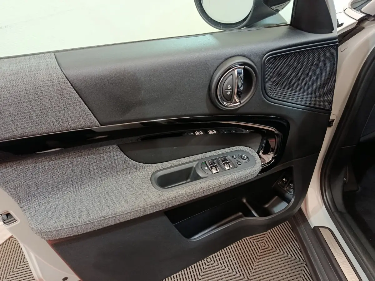 Intérieur côté conducteur du MINI Countryman blanc, montrant la porte avec commandes des vitres et tissu gris.