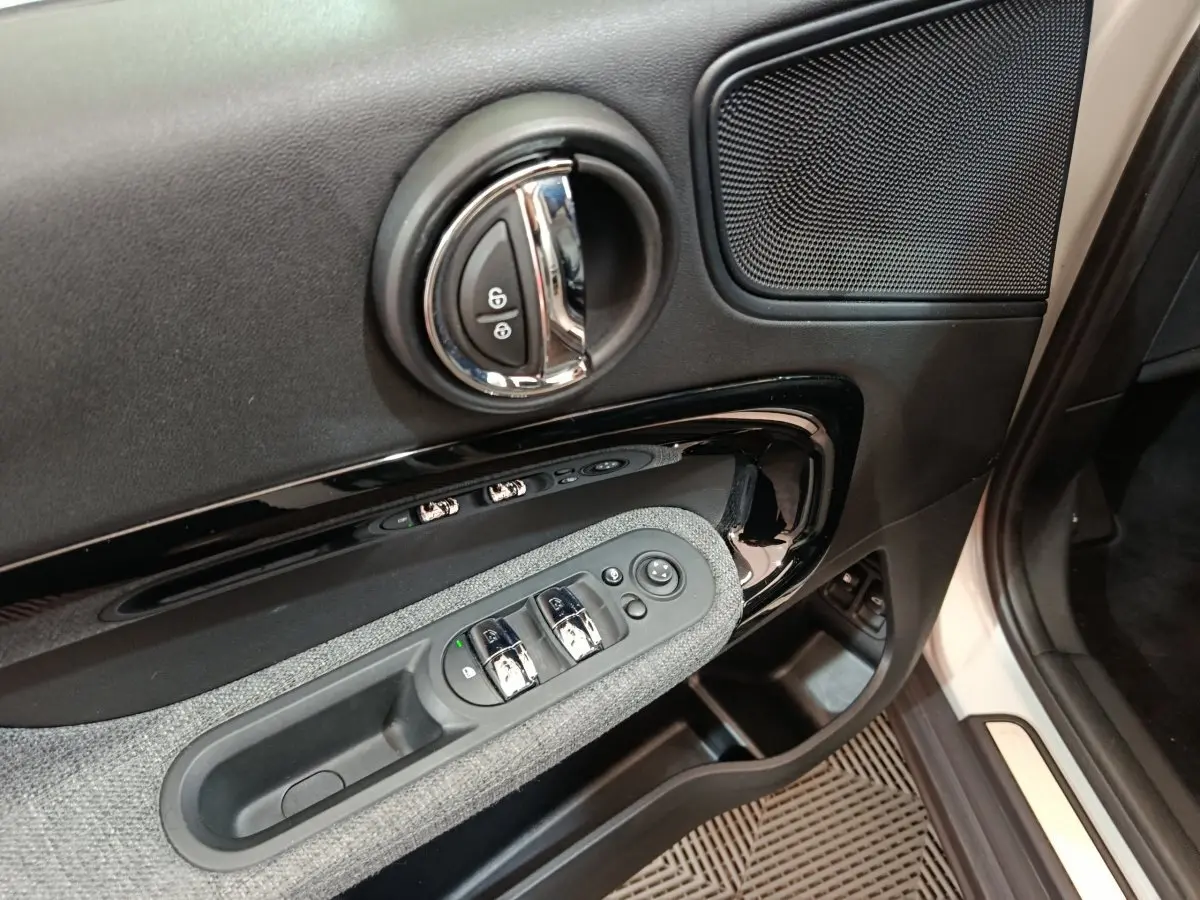 Vue rapprochée de la porte côté conducteur du MINI Countryman blanc, avec commandes de vitres et poignée chromée.
