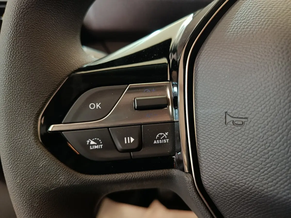 Gros plan sur les commandes gauche du volant noir du Peugeot Partner 2025, avec boutons de régulateur et assistant de conduite.