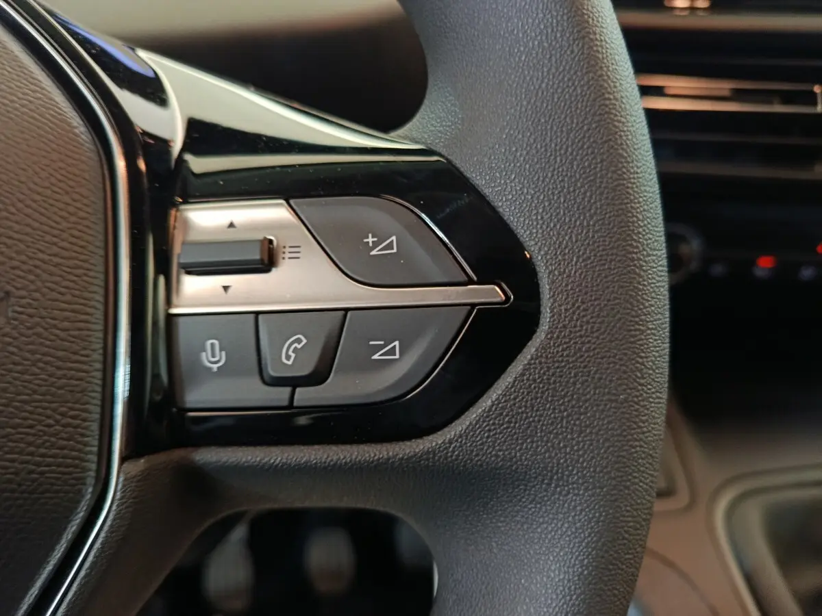 Gros plan sur les commandes noires et argentées au volant du Peugeot Partner blanc, côté gauche, intérieur moderne.