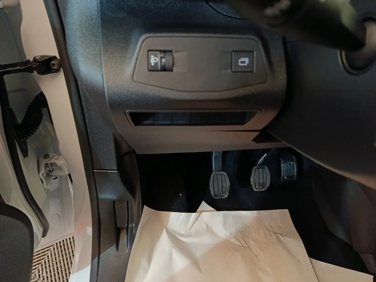 Vue intérieure en bas côté conducteur du Peugeot Partner blanc 2025, montrant les pédales et commandes sous le tableau de bord.