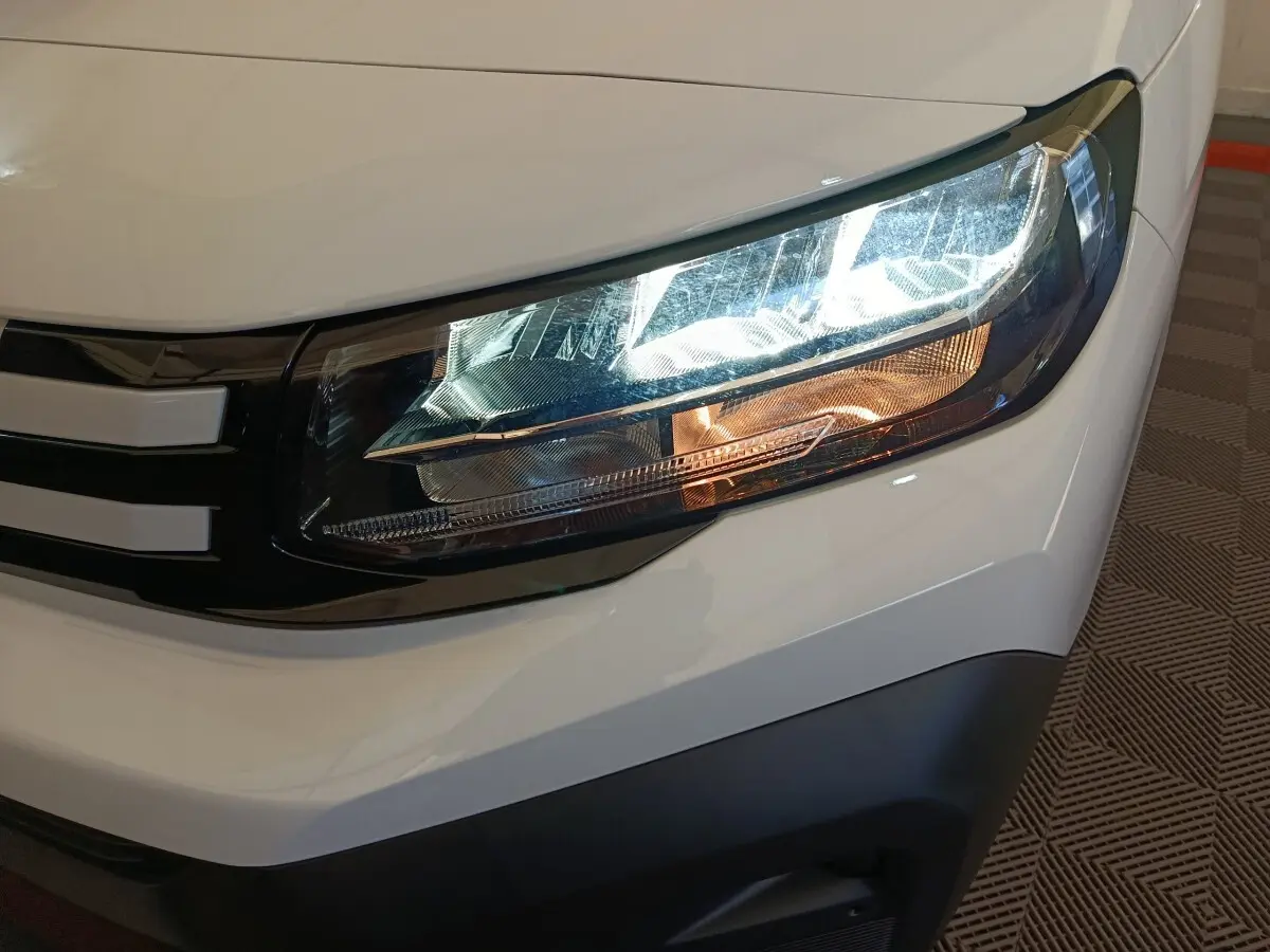 Gros plan sur le phare avant droit du Peugeot Partner blanc, mettant en valeur les détails modernes du bloc optique.