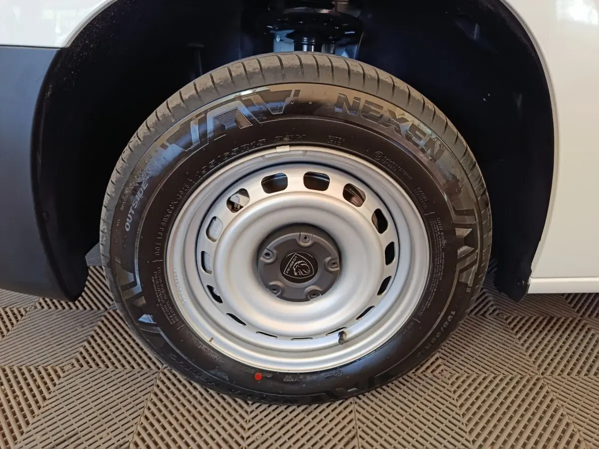 Gros plan sur la roue avant droite en acier gris du Peugeot Partner blanc, avec logo Peugeot au centre.