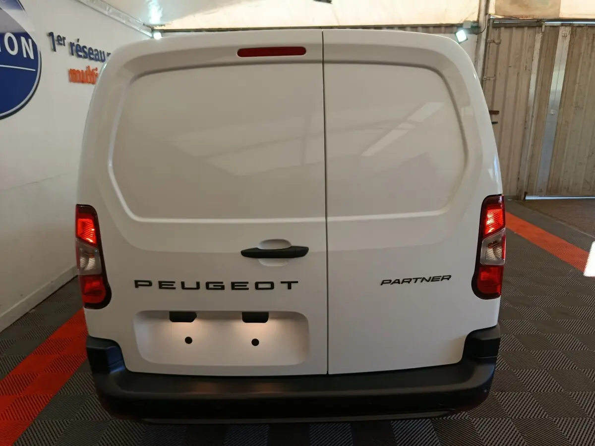 Vue arrière d’un utilitaire Peugeot Partner blanc avec portes battantes fermées et feux arrière allumés dans un garage.
