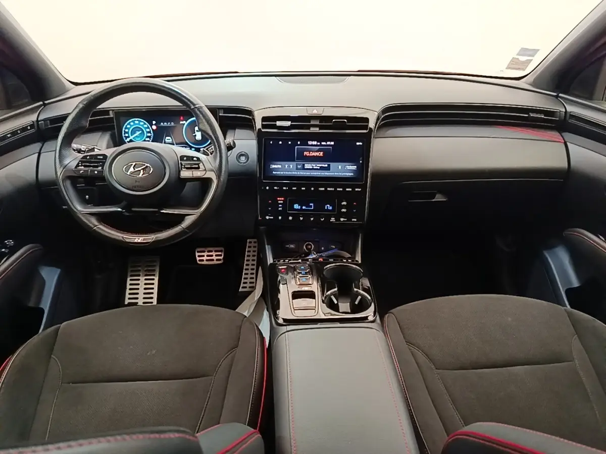 Vue intérieure frontale du Hyundai Tucson N Line 2022, tableau de bord noir avec écran tactile central et volant cuir multifonctions.