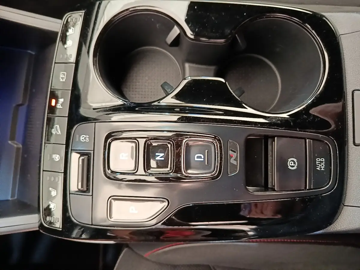 Vue rapprochée de la console centrale noire avec commandes de boîte auto et deux porte-gobelets du Hyundai Tucson rouge.