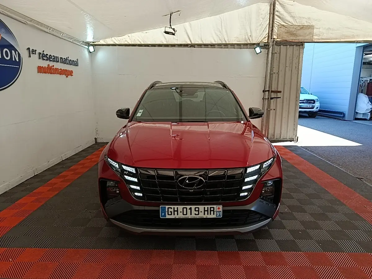 Vue frontale d'un Hyundai Tucson rouge 2022 avec calandre noire et feux LED distinctifs allumés.