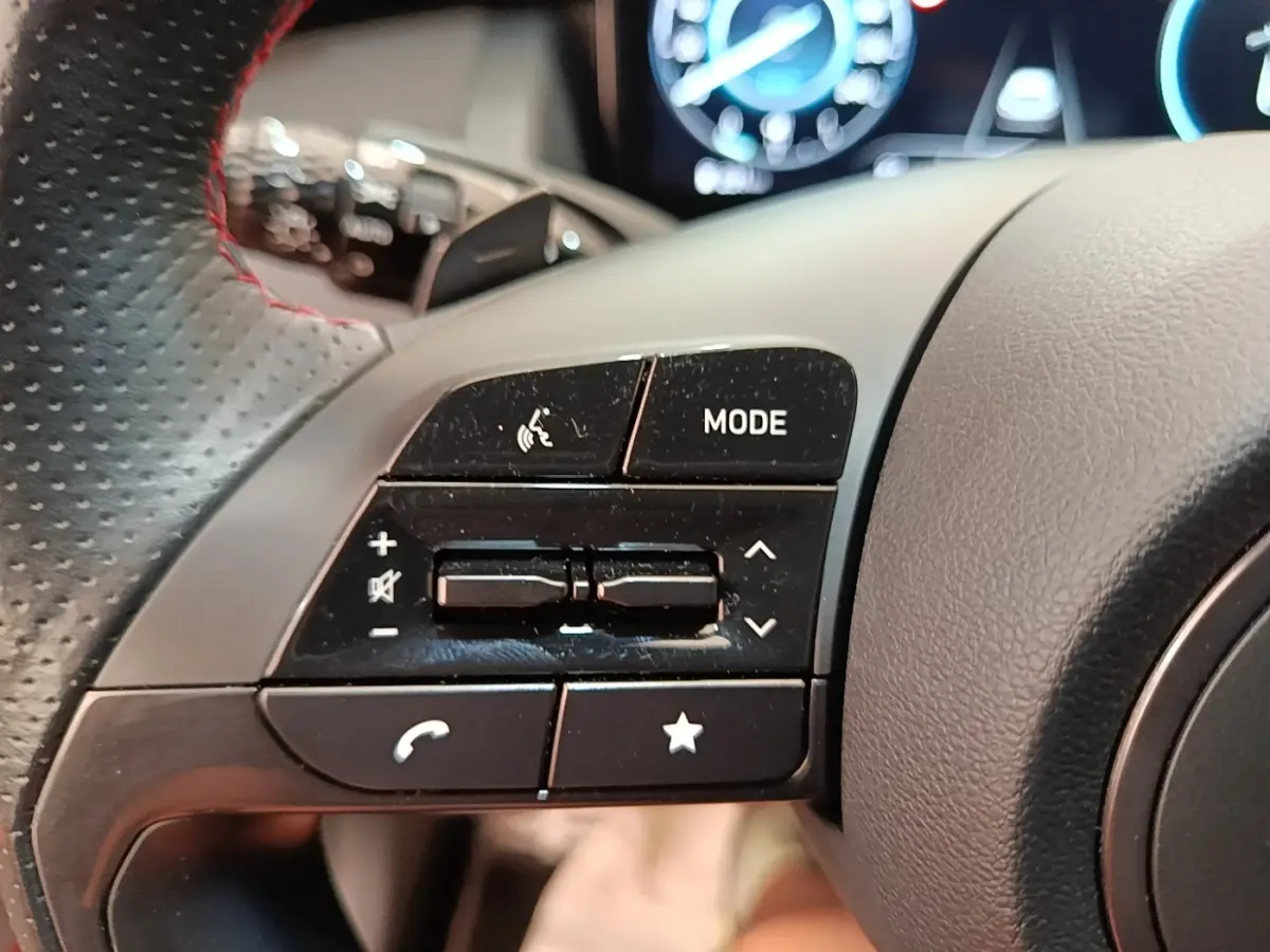 Gros plan sur les commandes multifonctions noires du volant cuir perforé côté gauche du Hyundai Tucson rouge 2022.