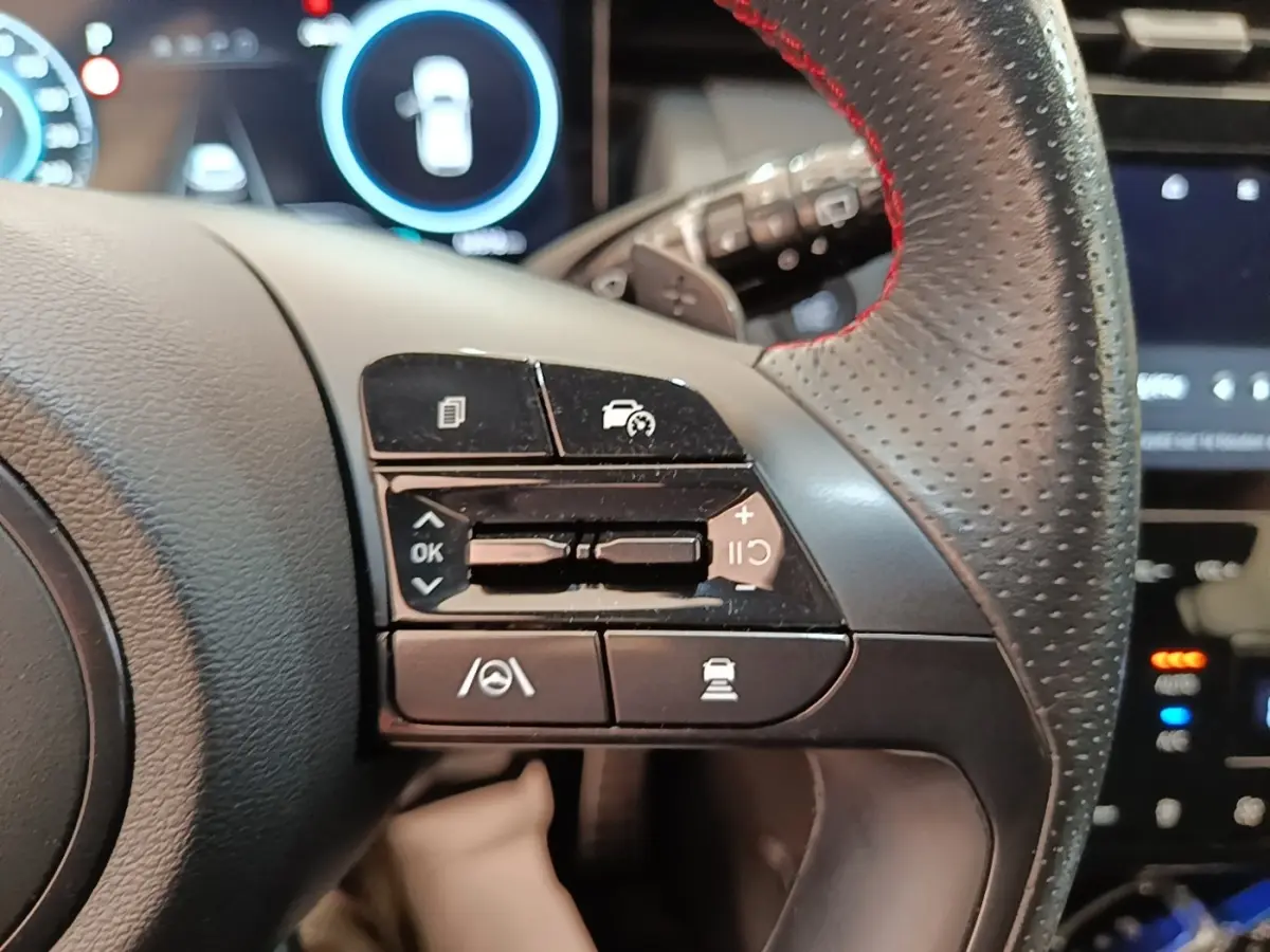 Gros plan sur les commandes multifonctions à gauche du volant cuir perforé rouge du Hyundai Tucson rouge 2022.