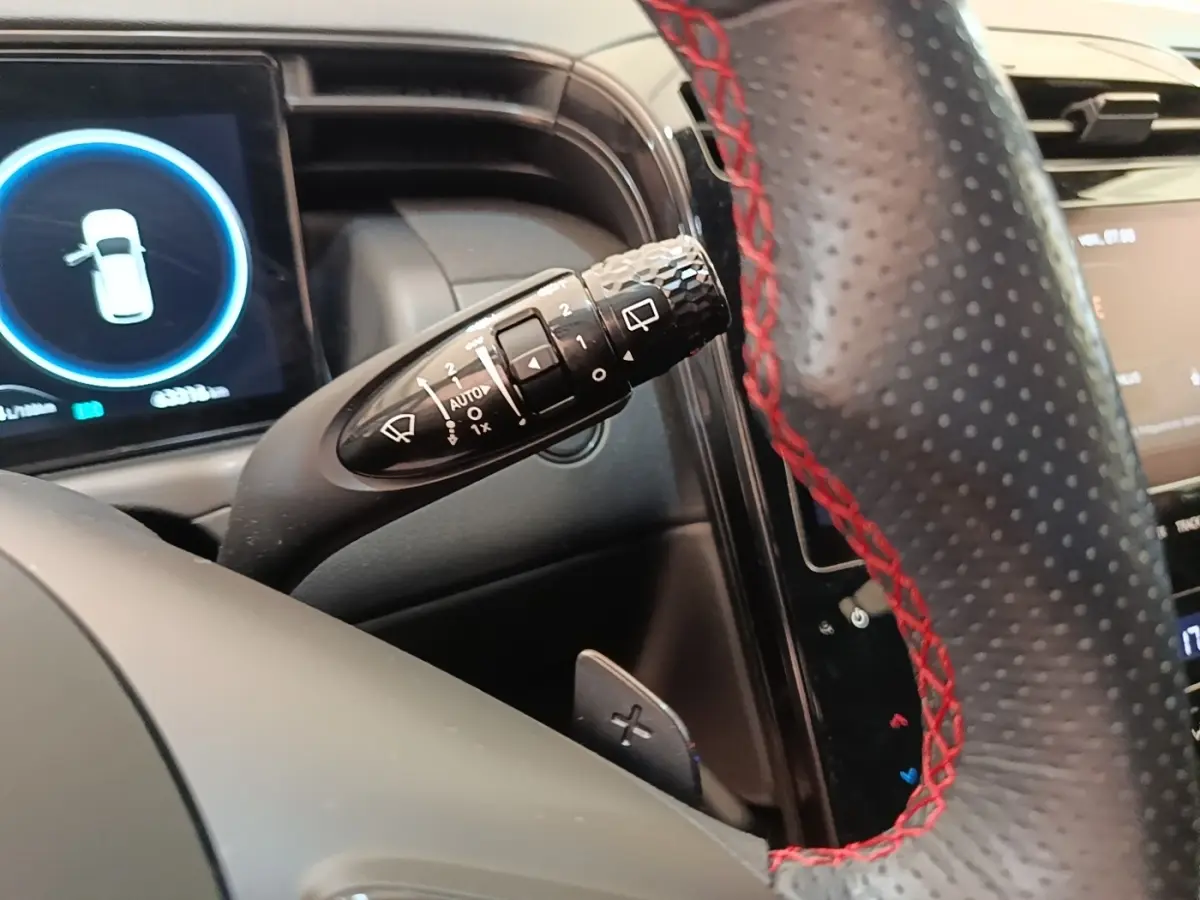 Gros plan sur la commande d’essuie-glace à gauche du volant perforé noir avec surpiqûres rouges du Hyundai Tucson rouge 2022.