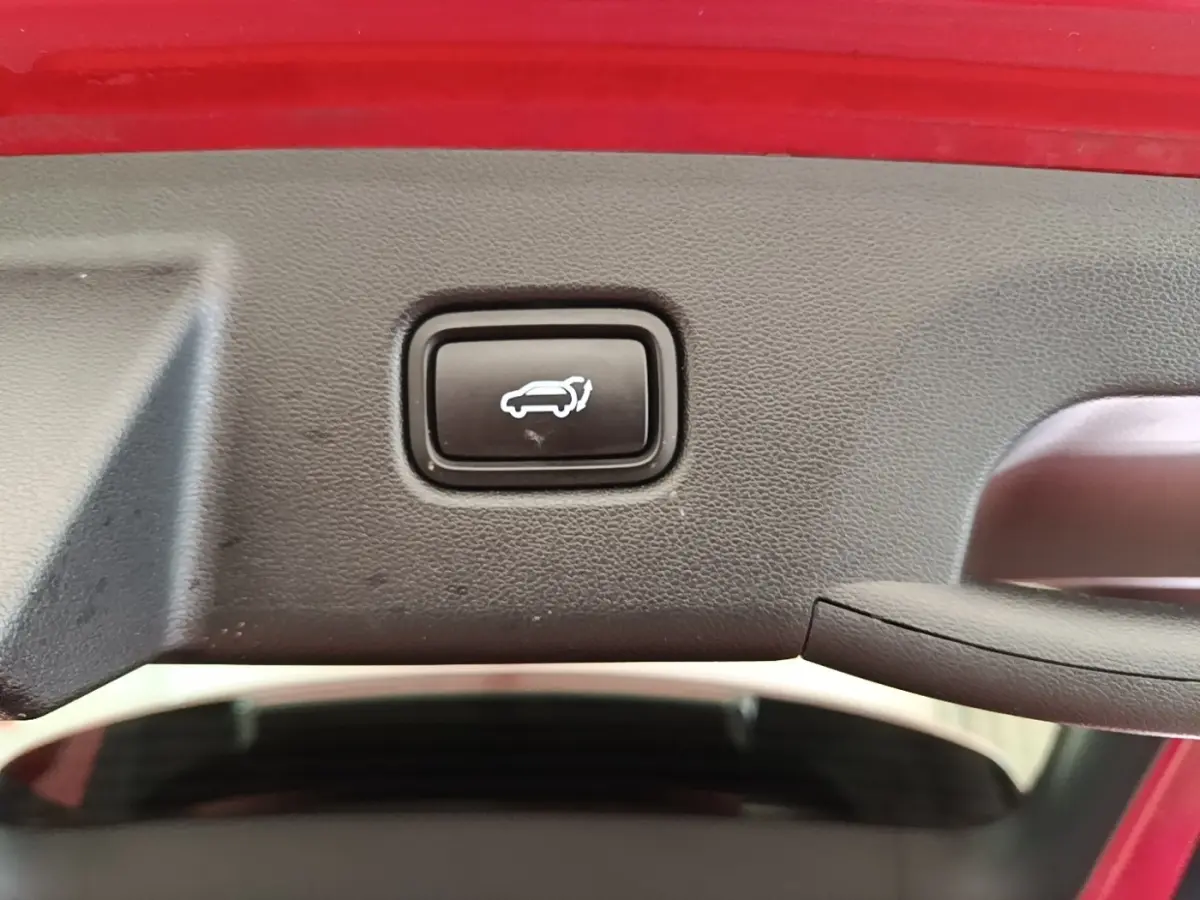 Bouton d'ouverture électrique du coffre sur le hayon intérieur d'un Hyundai Tucson rouge, vue rapprochée.