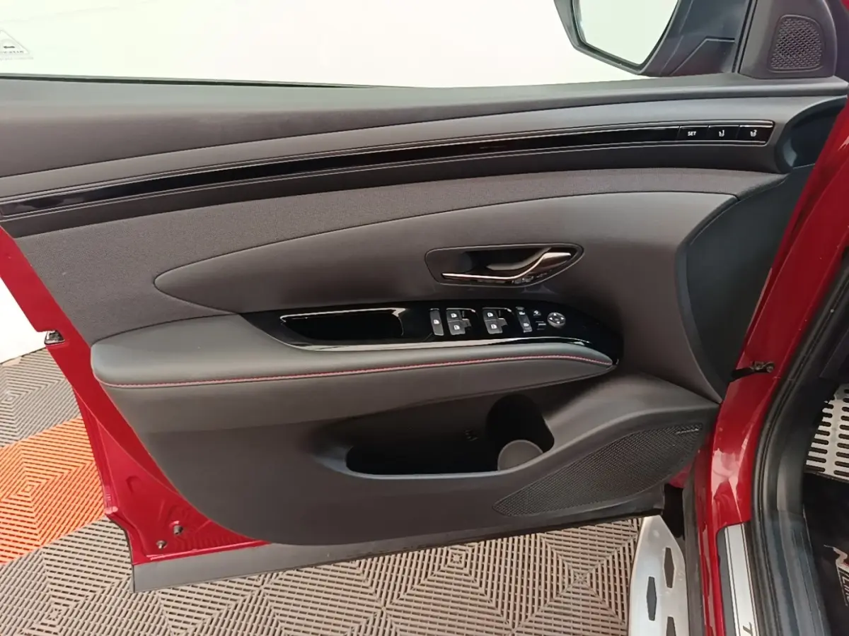 Vue intérieure de la porte avant gauche rouge du Hyundai Tucson 2022 avec commandes électriques et surpiqûres rouges.