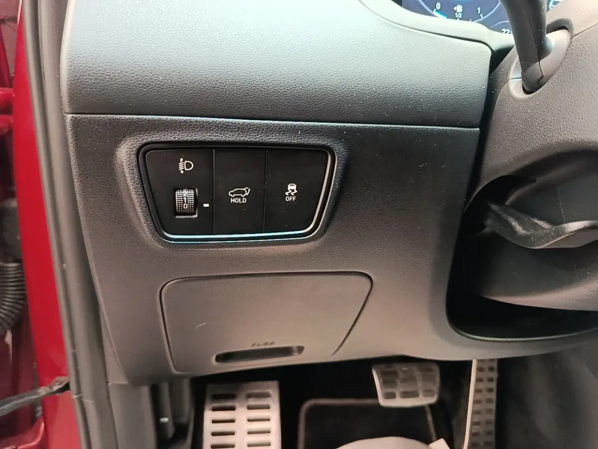 Détail intérieur côté gauche tableau de bord rouge Hyundai Tucson 2022 avec commandes éclairage et maintien frein.