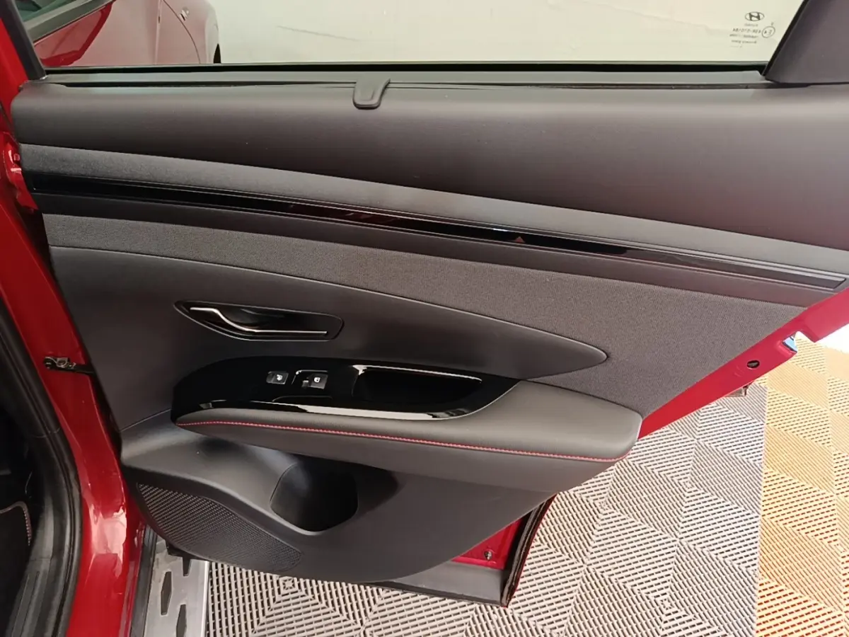 Vue intérieure de la porte arrière gauche rouge du Hyundai Tucson 2022 avec commandes de fenêtre et surpiqûres rouges.