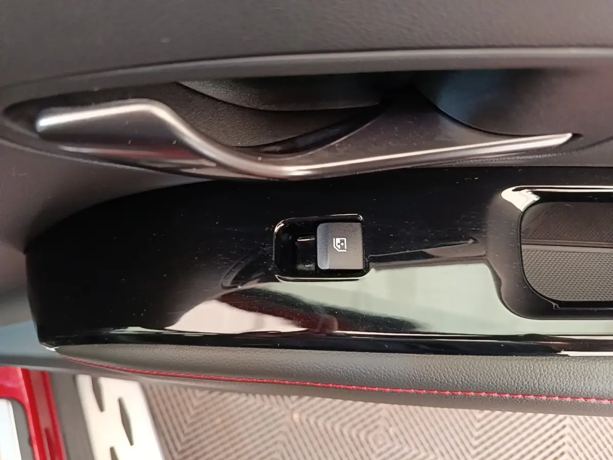 Détail de la commande de verrouillage électrique sur la porte intérieure noire avec surpiqûres rouges du Hyundai Tucson rouge.
