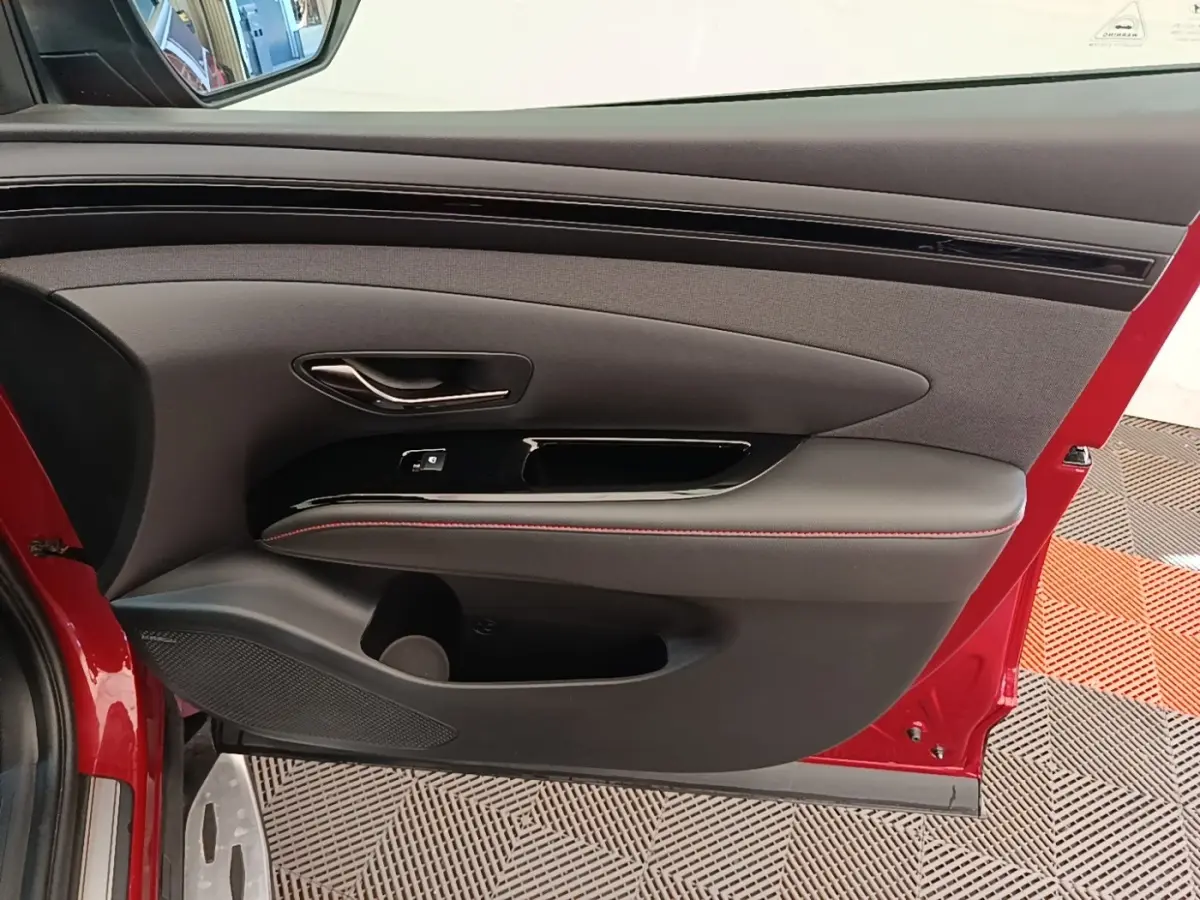 Intérieur côté gauche de porte rouge Hyundai Tucson 2022, avec garniture noire et surpiqûres rouges.