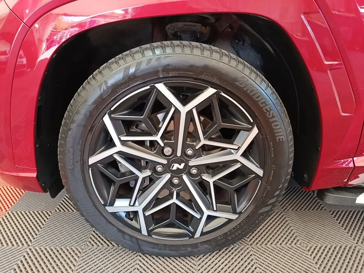 Gros plan sur la roue avant droite du Hyundai Tucson rouge, jante alliage noire et argentée au design géométrique N Line.
