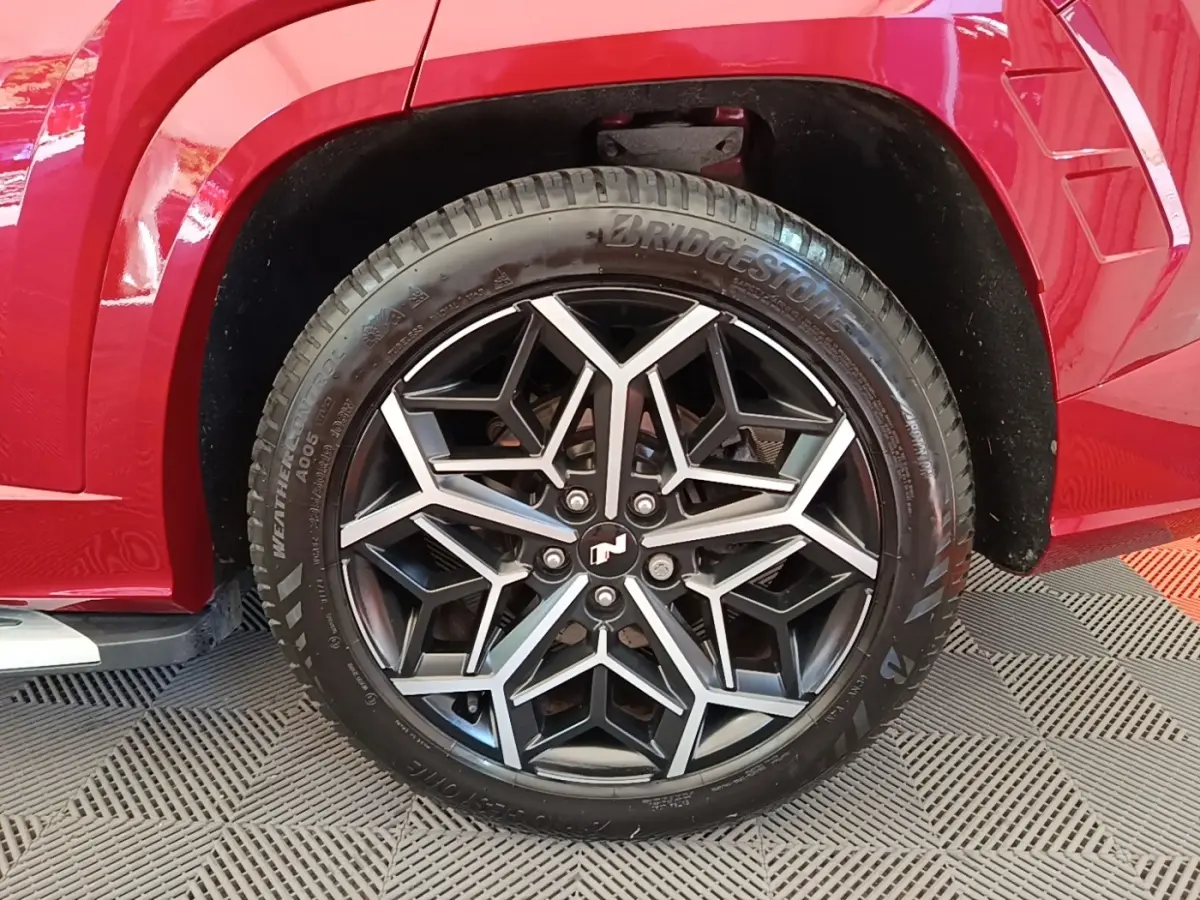 Gros plan sur la roue avant droite du Hyundai Tucson rouge 2022, mettant en valeur la jante noire et argentée au design géométrique.