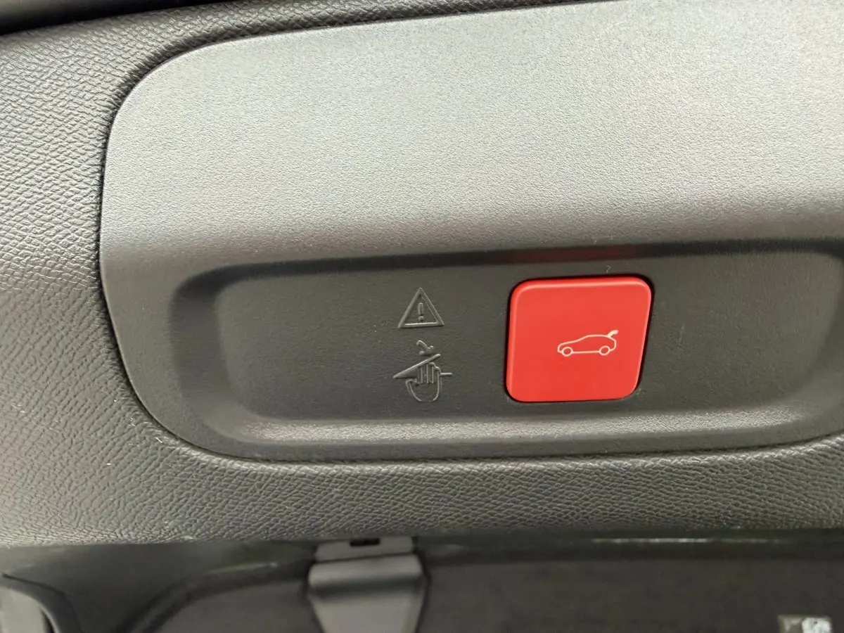 Gros plan sur le bouton rouge d'ouverture électrique du coffre dans l'habitacle d'une Peugeot 408 PHEV 225 GT.