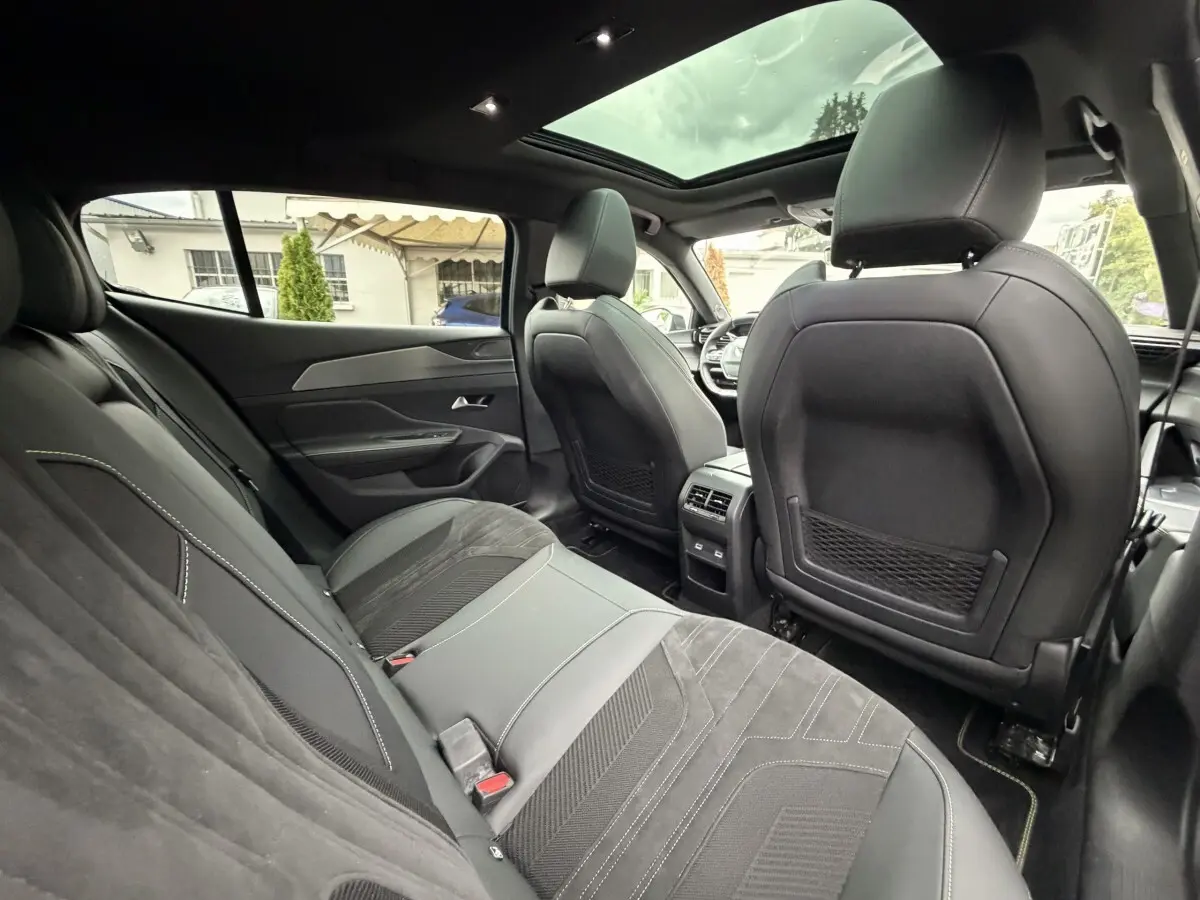 Intérieur arrière de la Peugeot 408 PHEV 225 GT 2023, sièges noirs, toit panoramique et tableau de bord visible en avant.