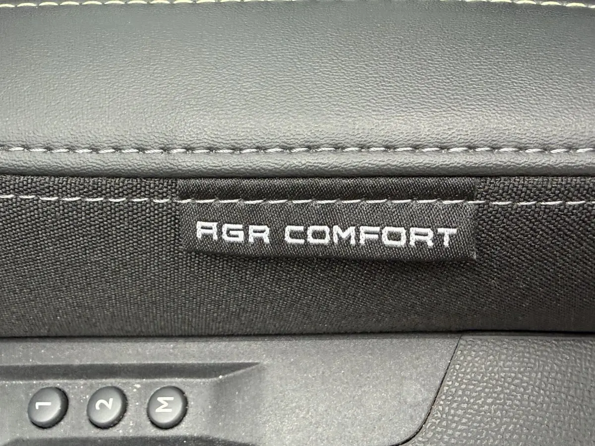 Détail intérieur montrant l'étiquette AGR Comfort sur siège tissu noir avec commandes mémoire de réglage.