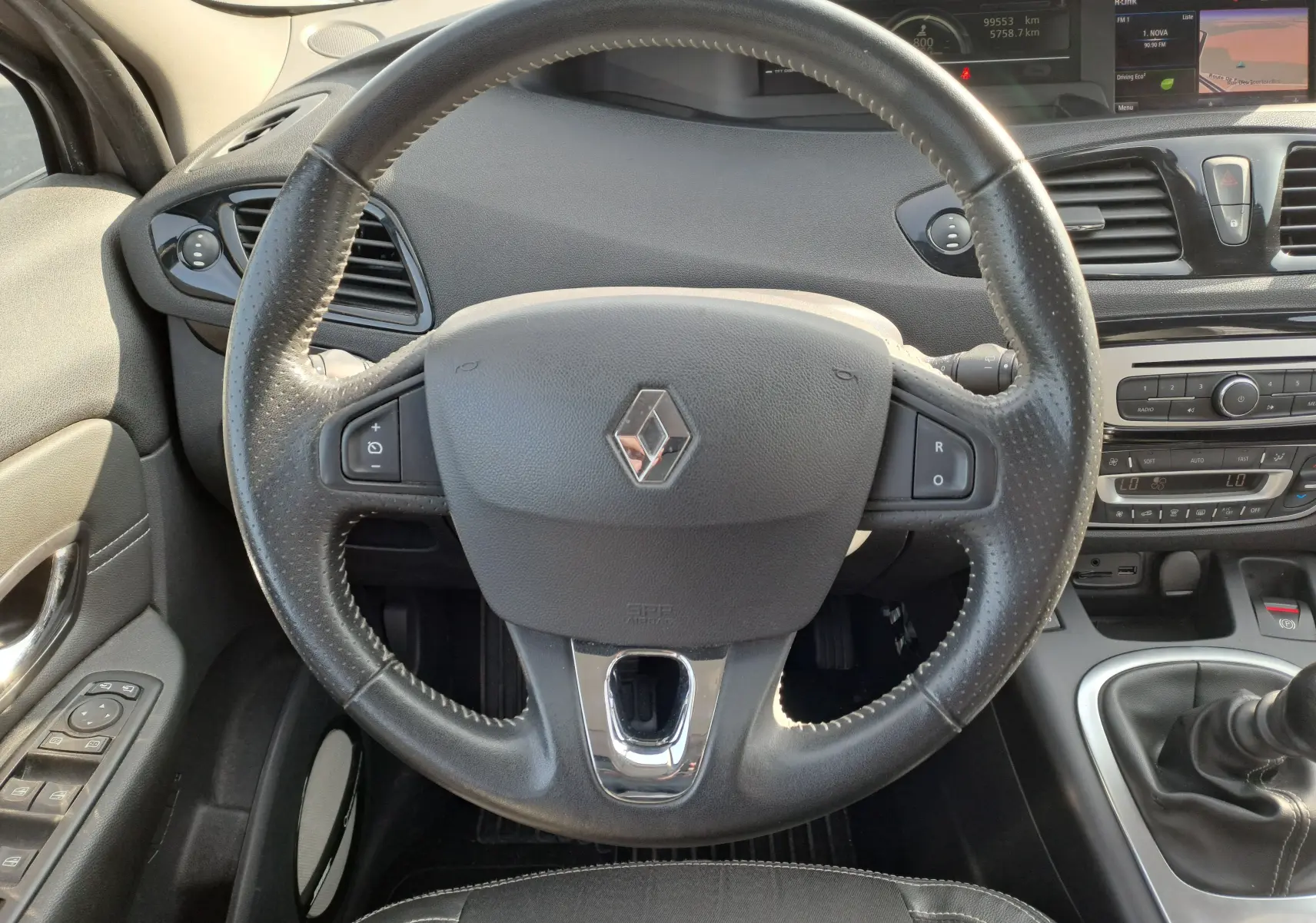 Vue rapprochée du volant en cuir noir avec logo Renault, tableau de bord et levier de vitesses d'une Renault Scenic III gris 2016.