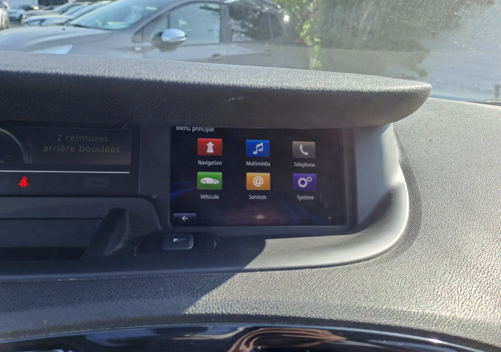 Écran central tactile du tableau de bord du Renault Scénic III gris, affichant le menu principal multimédia en plein jour.
