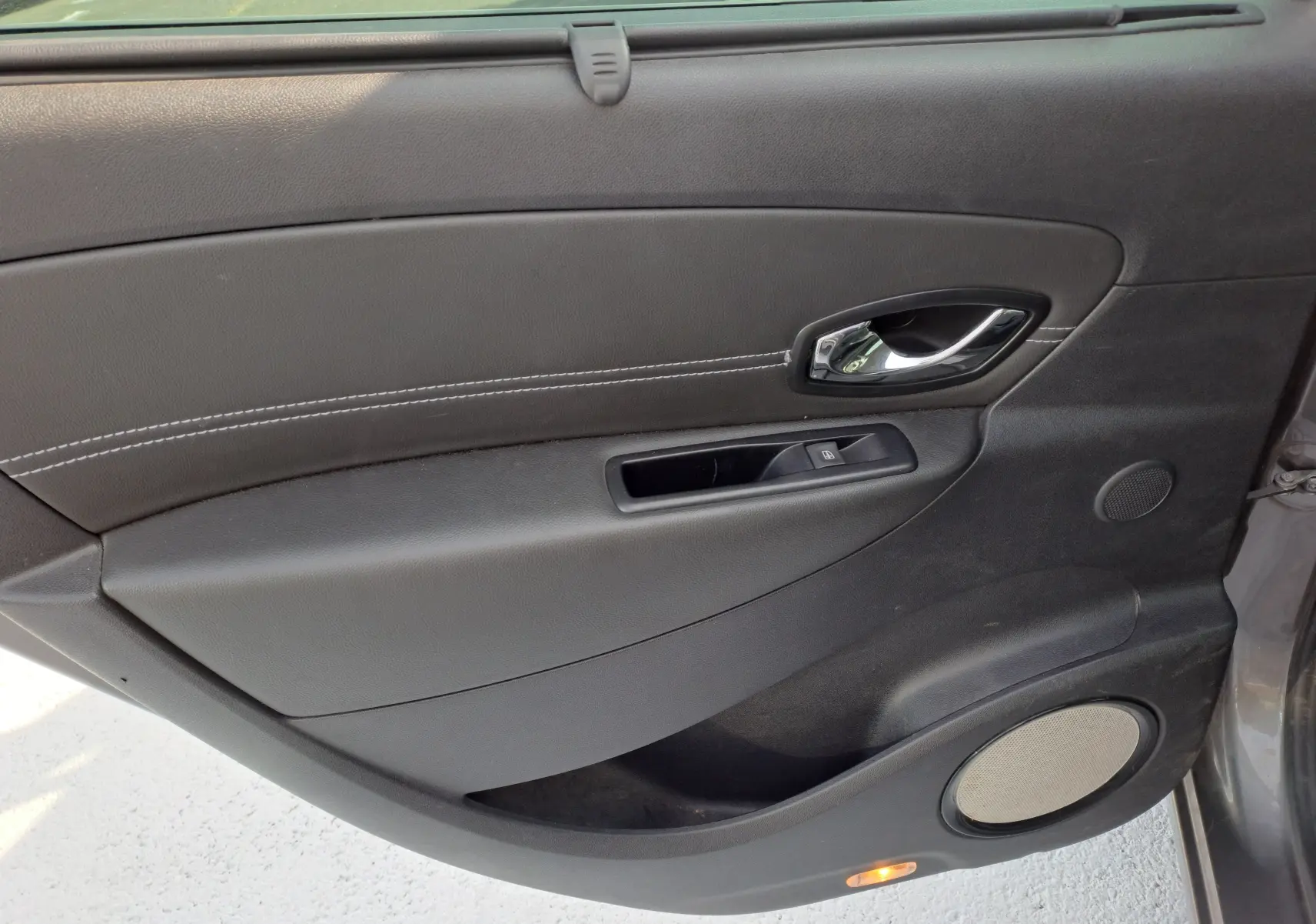 Porte intérieure côté gauche de Renault Scenic III gris 2016, avec poignée chrome et haut-parleur intégré.