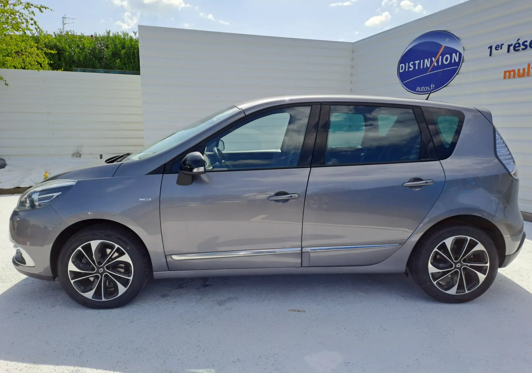 Profil côté gauche d’un Renault Scénic III gris 2016 avec jantes alliage et vitres teintées sur fond clair.