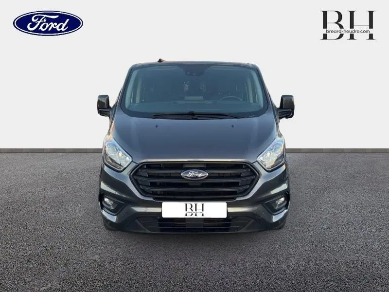 Vue de face du Ford Transit Custom Fourgon gris Magnétic métallisé avec calandre noire et phares allumés.