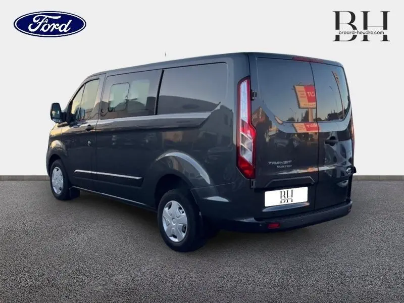 Vue 3/4 arrière droite d'un Ford Transit Custom Fourgon gris métallisé avec portes battantes arrière et vitres latérales teintées.