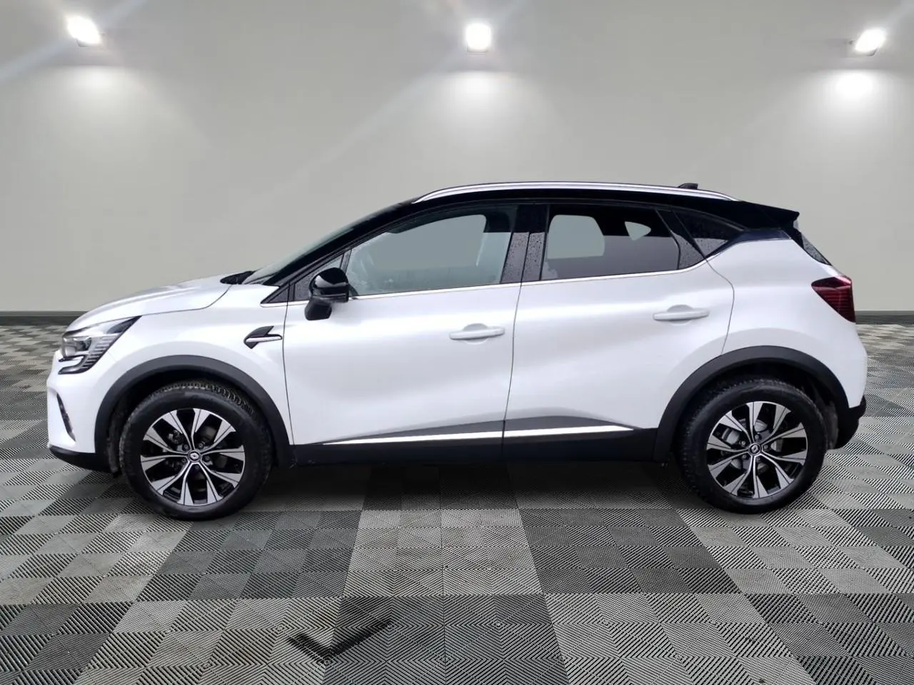 Profil droit du Renault Captur blanc 2024 avec toit noir et jantes alliage bicolores sur fond neutre.