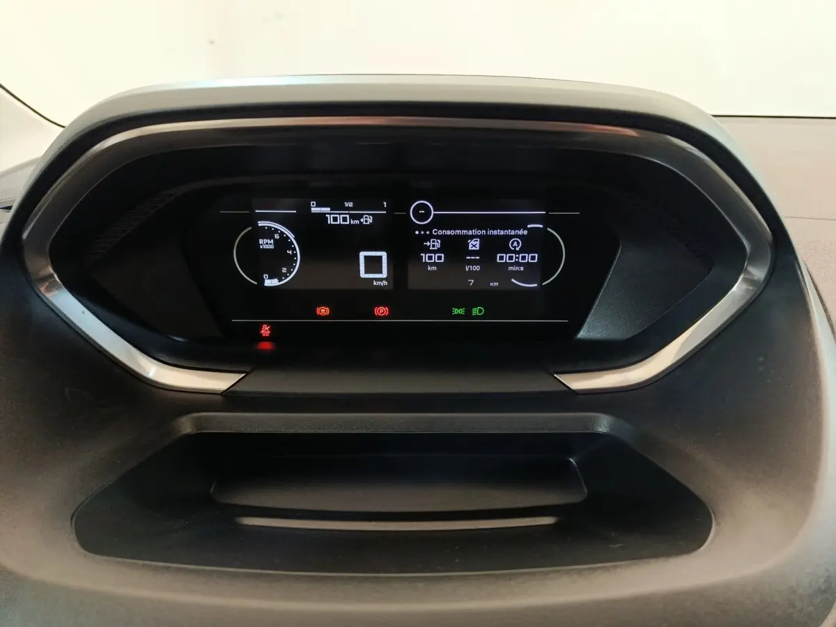 Vue rapprochée du tableau de bord numérique du Peugeot Partner blanc 2025, affichant la consommation instantanée et les alertes.