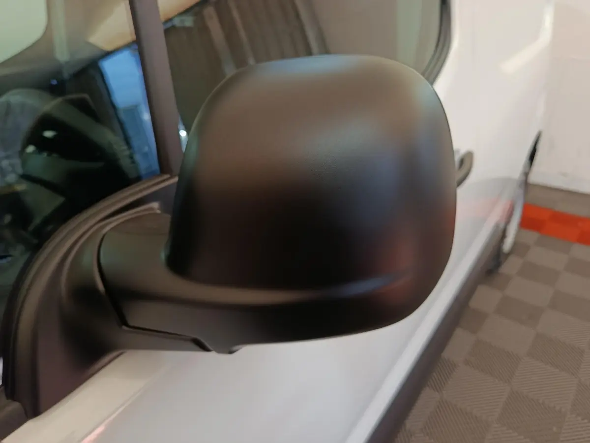 Rétroviseur noir en gros plan sur le côté gauche d’un Peugeot Partner blanc vu de profil avant.