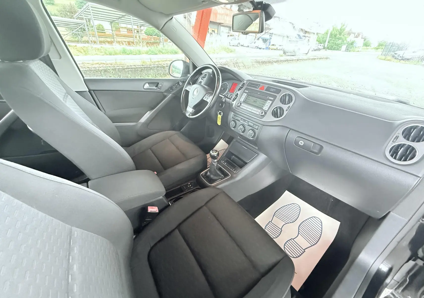 Vue intérieure côté conducteur du Volkswagen Tiguan noir 2007, montrant sièges tissu noirs et tableau de bord avec boîte manuelle.