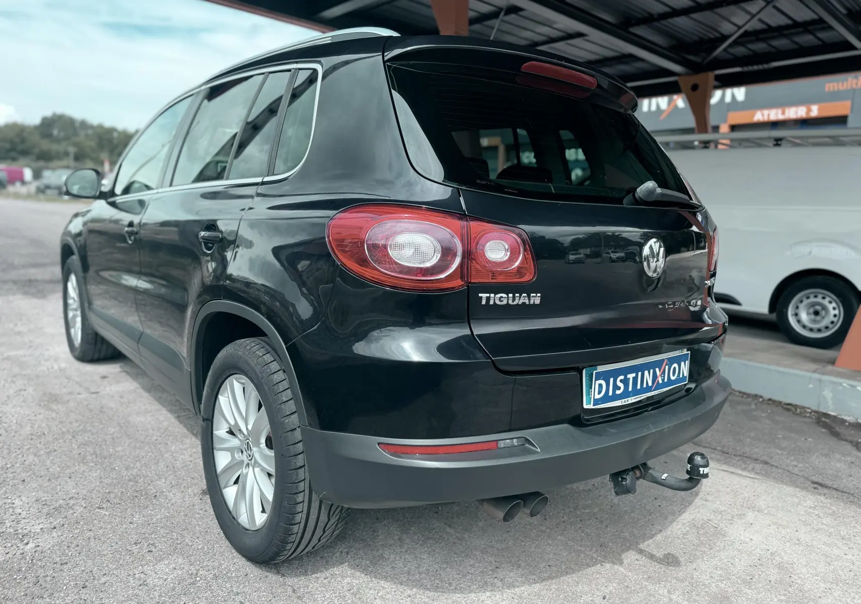 Vue 3/4 arrière droite d’un Volkswagen Tiguan noir avec attelage de remorque, sous un abri extérieur.