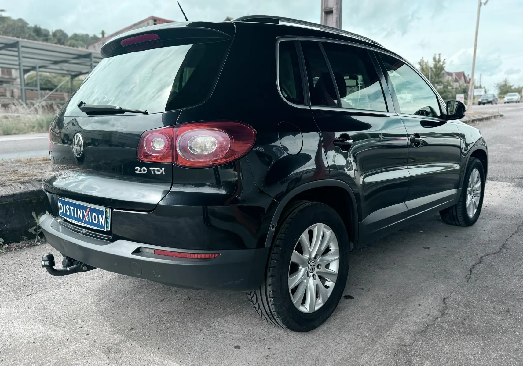 Vue 3/4 arrière droite d'un Volkswagen Tiguan noir avec attelage et jantes alliage sur route urbaine.