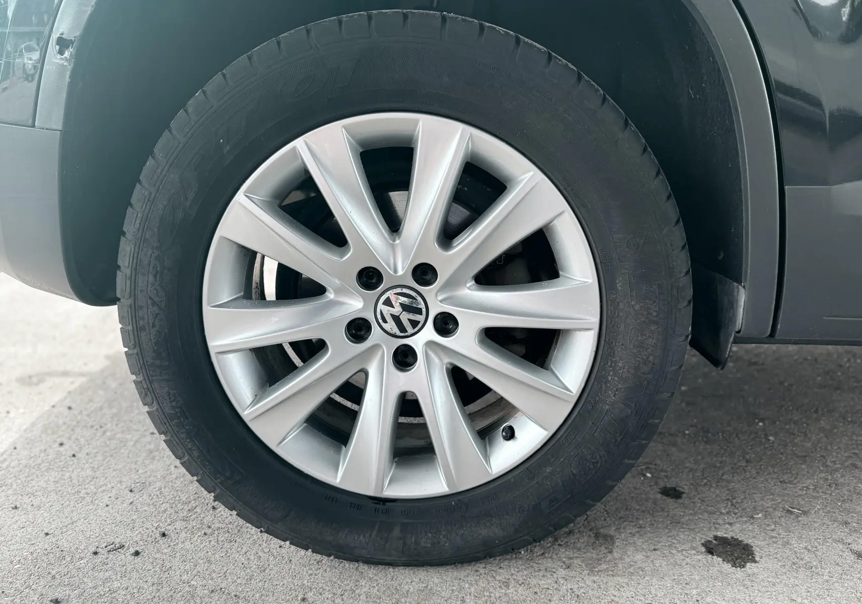 Gros plan sur la roue avant gauche avec jante argentée et logo Volkswagen sur un Volkswagen Tiguan noir.