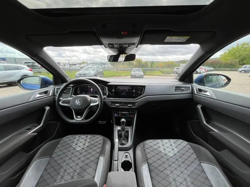 Vue intérieure avant du Volkswagen Taigo 1.5 TSI R-Line 2023, sièges sport et toit ouvrant panoramique en verre visible.