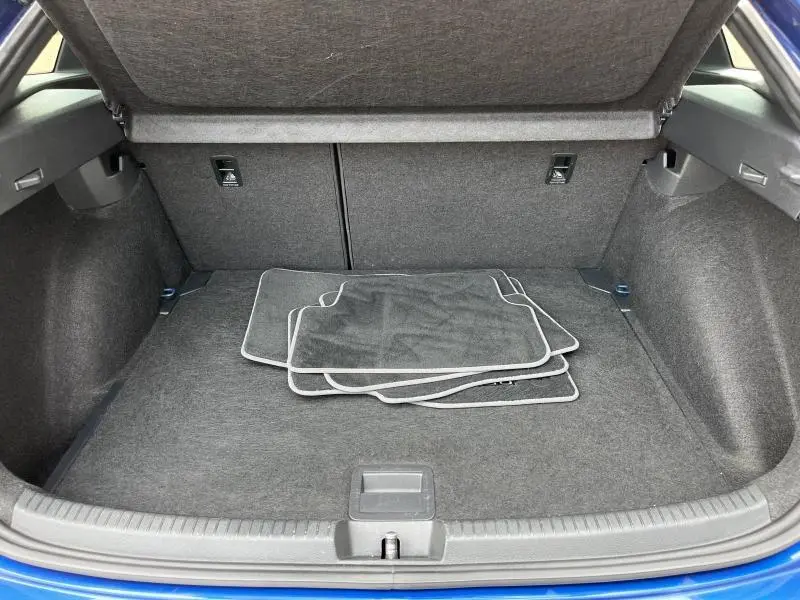 Coffre ouvert du Volkswagen Taigo bleu récif, montrant un espace de chargement avec tapis de sol gris.