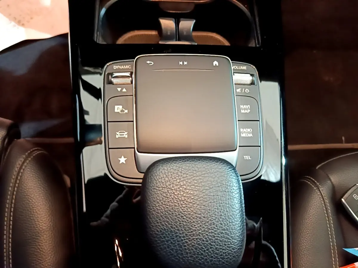 Gros plan sur la console centrale noire brillante et le pavé tactile avec repose-poignet cuir dans une Mercedes Classe A gris foncé.