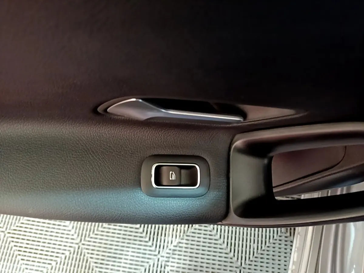 Gros plan sur la poignée intérieure et le bouton de verrouillage de la porte côté conducteur d'une Mercedes Classe A gris foncé.
