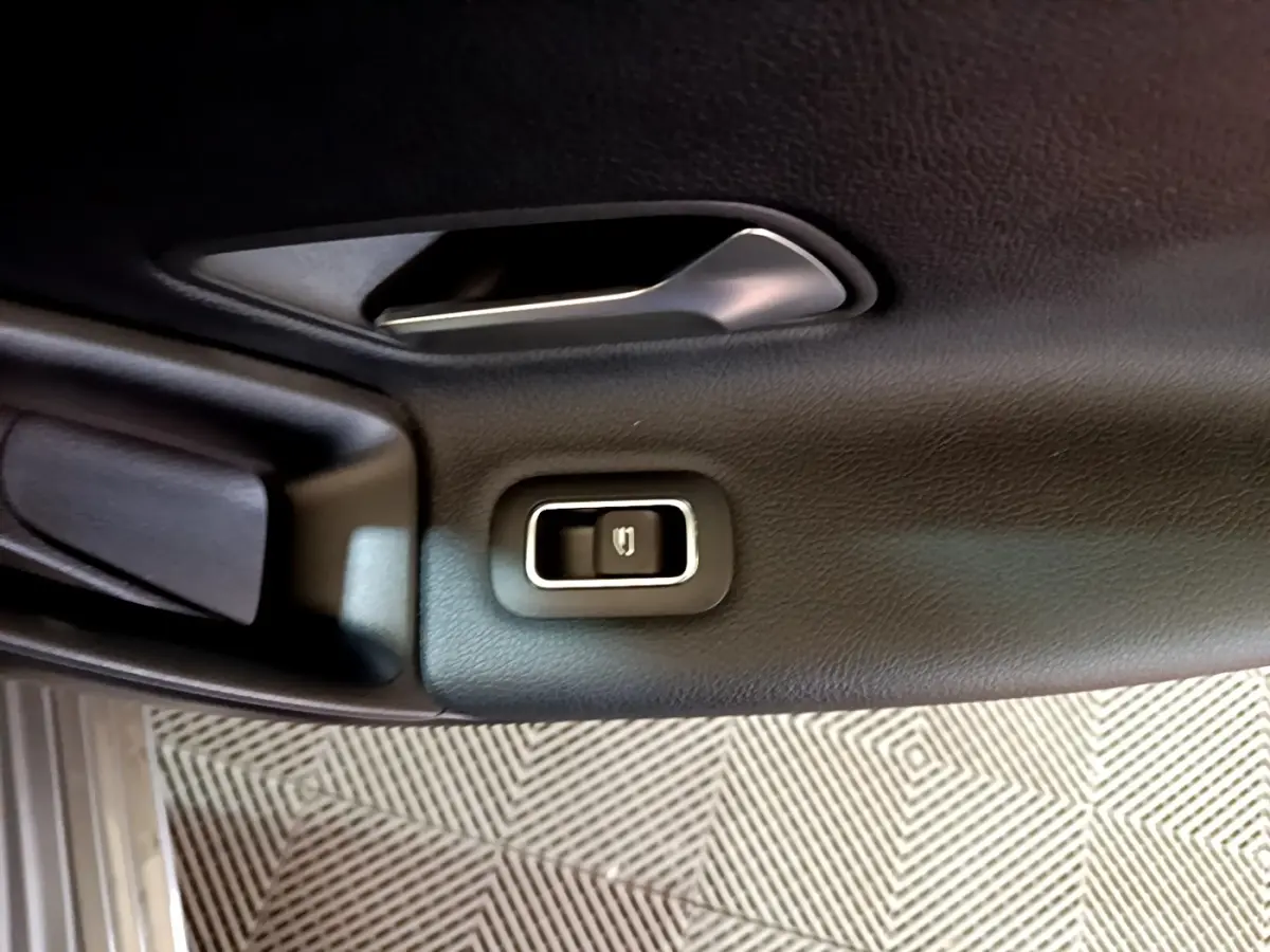 Détail du bouton de verrouillage électrique sur la porte intérieure noire d’une Mercedes Classe A gris foncé.