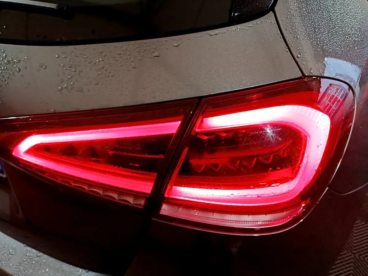 Gros plan sur le feu arrière droit allumé d’une Mercedes Classe A gris foncé sous la pluie.