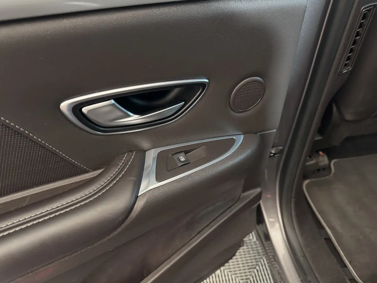 Gros plan sur la poignée intérieure et la commande de vitre côté arrière droit d'une Renault Espace gris foncé.