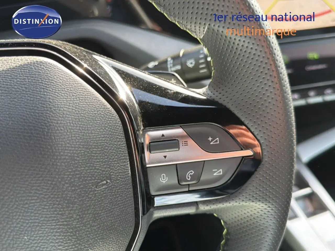 Gros plan sur les commandes multifonctions du volant en cuir perforé d'une Peugeot 408 gris selenium metal.